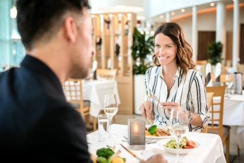 Ein Mann und eine Frau sitzen sich im Innenbereich des Restaurants Fontäne gegenüber und blicken sich an, während sie ihr Essen zu sich nehmen.