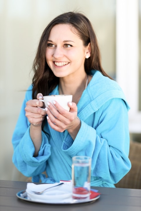 Eine junge Dame sitzt in blauem Bademantel im Café Promenade und hält eine Tasse Kaffee in der Hand.