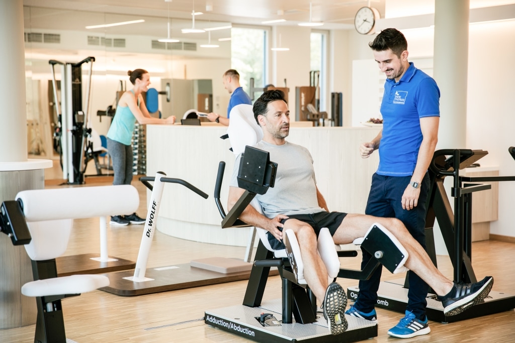 Ein Physiotherapeut erklärt einem trainierenden Mann ein Trainingsgerät.