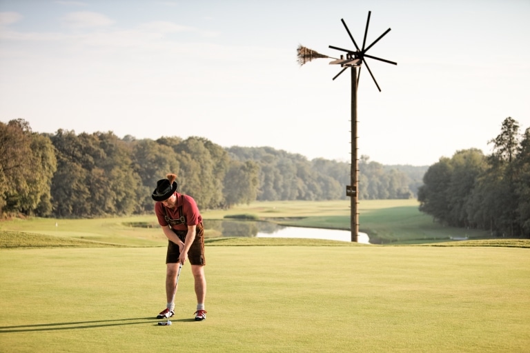 Ein Mann steht auf einem Golfplatz und hält den Golfschläger zum auf der Wiese liegenden Golfball.