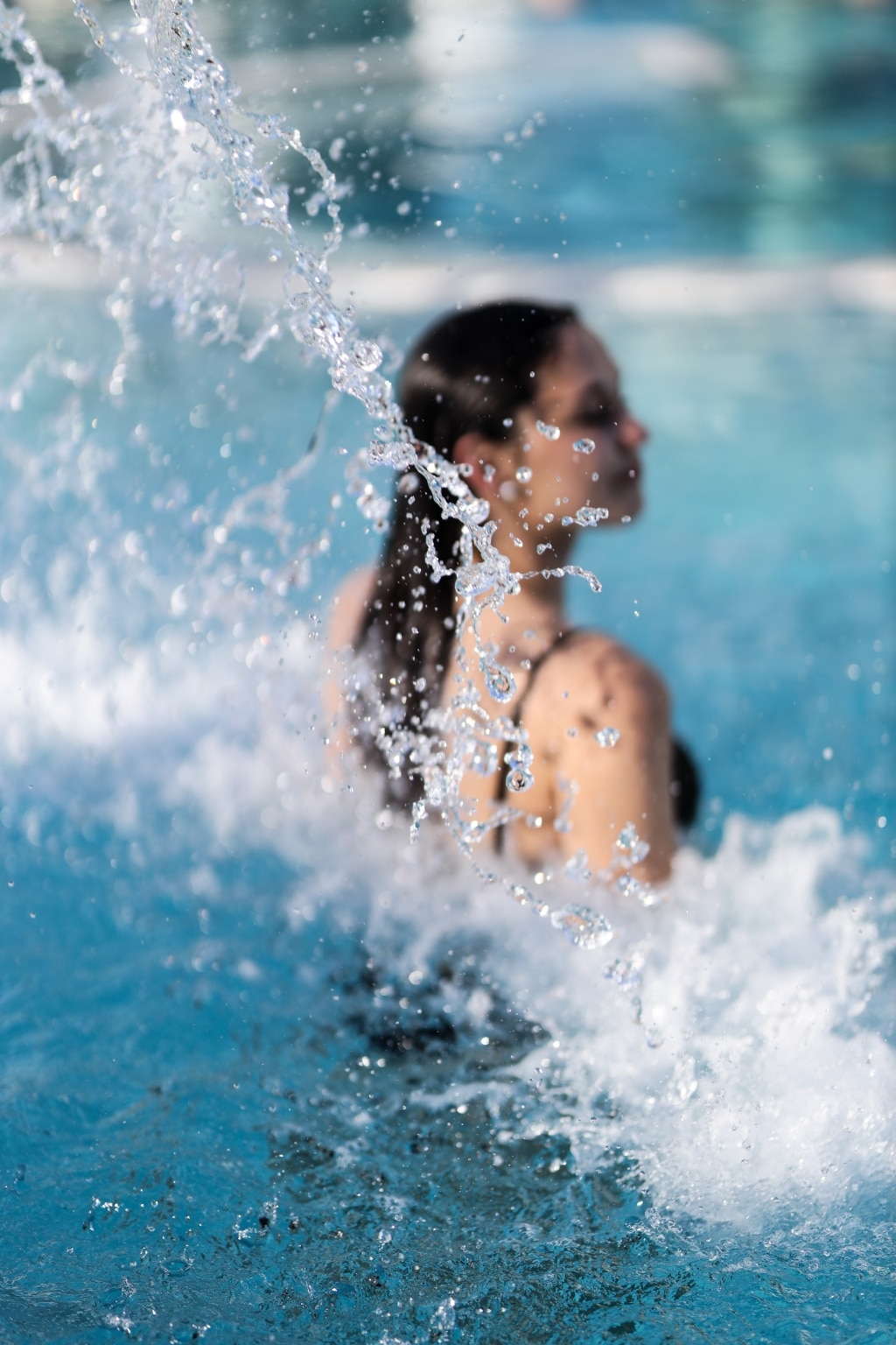 Eine junge Frau steht in einem Thermalwasserbecken der Parktherme und lässt von hinten einen Wasserfall auf sich herabprasseln.