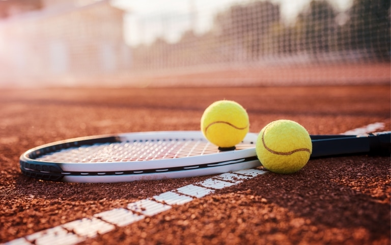 Ein Schläger und zwei Tennisbälle liegen auf einem Tennisplatz.