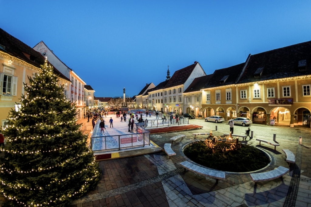 Blick auf den winterlichen Bad Radkersburger Hauptplatz mit Eislaufplatz, der von zahlreichen Menschen bevölkert wird.