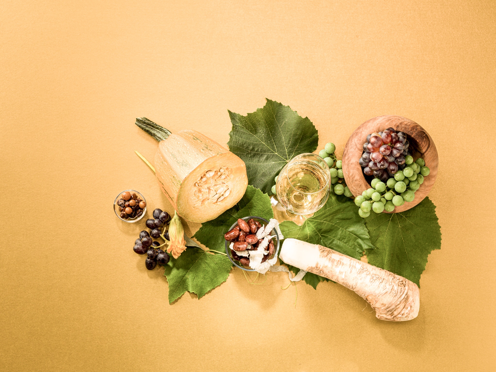 Zu sehen sind regionale Köstlichkeiten aus dem Thermen- und Vulkanland, etwa Weintrauben, Kren, Käferbohnen und ein Achterl Wein.