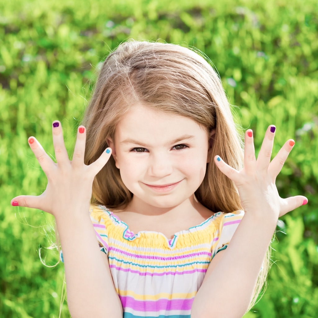 Ein junges Mädchen hält seine Hände mit lackierten Fingernägeln in die Kamera.